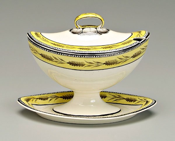 Creamware sauce tureen,: almond shaped tureen with conforming attached under plate, finely decorated with wheat borders on mustard yellow ground, British, early 19th century, 6 x 8 in. Lid with 3 in. crack, 1/2 in. rim crack,