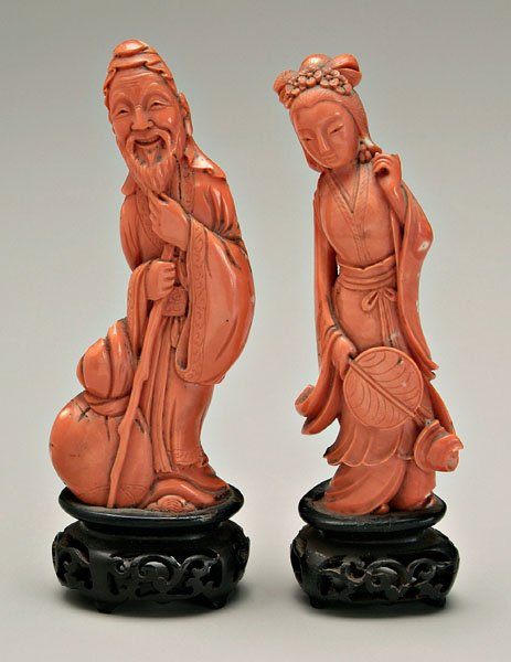 Two Chinese carved coral figures:: elderly smiling man stroking beard, a bag at his feet, 4-3/4 in., 5-3/4 in. on fitted wood stand; elegantly coiffed and dressed lady holding a fan in her right hand, 4-3/4 in., 5-3/4 in. fitted wood s