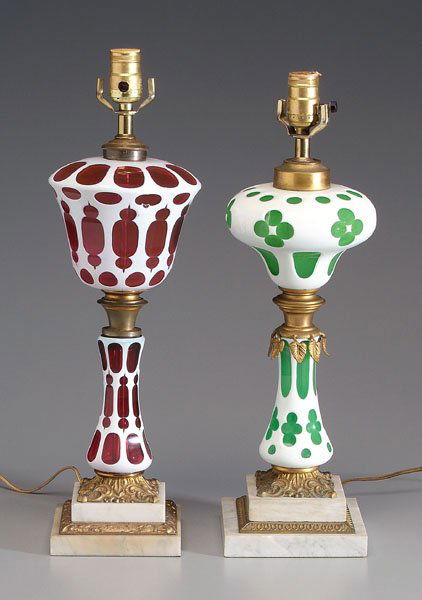 Two ormolu-mounted lamps,: cased glass: white cut to ruby, 17 in. to bottom of fixture; white cut to emerald, 16-1/2 in. to bottom of fixture, both with stepped ormolu-mounted marble bases. Later electrification, bases with min