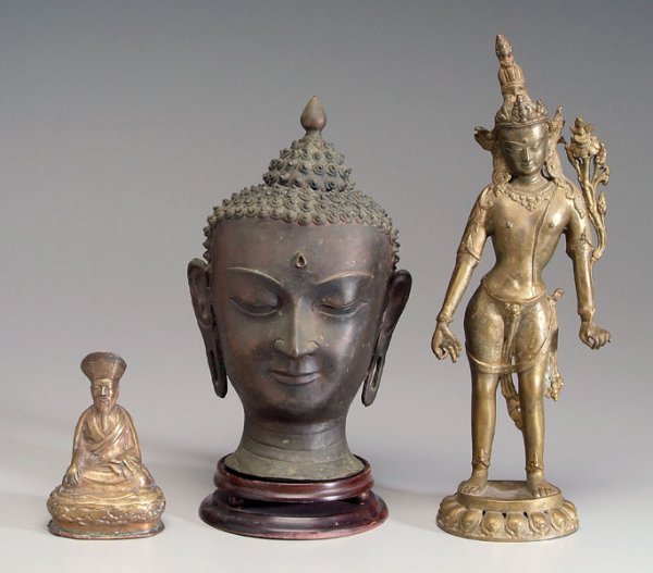 Three Buddhist figures:: bronze Thai Buddha head, 13-1/2 in. with later wood stand, [possibly lacking insert;] brass Indian attendant figure standing on lotus throne, 17-1/4 in.; bronze Tibetan lama seated on a lotus throne, 