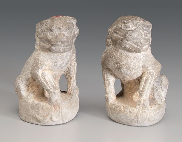 Pair Chinese Buddhist lions:: carved gray stone, mirror image of head turned to side, on circular bases, each with red export seal, 19th or 20th century, 14 in. Each with losses, one with repairs at muzzle.