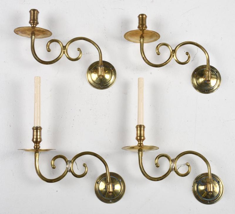 Group of Four Reproduction Brass Sconces: with ribbed nozzles above a circular drip pan, scrolled arms and circular back plates, two wired for electricity with plastic candles, height 9 in. - Provenance: Property from the Collection of Dudley