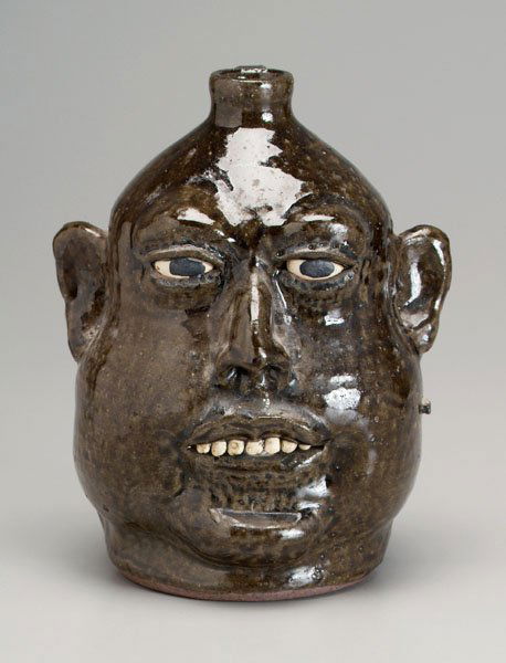 Lanier Meaders stoneware face jug: (White County, Georgia, 1917-1998), runny dark olive alkaline glaze, ceramic teeth, base marked "Lanier Meaders 1-1-81", 9-1/2 in. Excellent condition, surface anomalies including kiln debris as made.