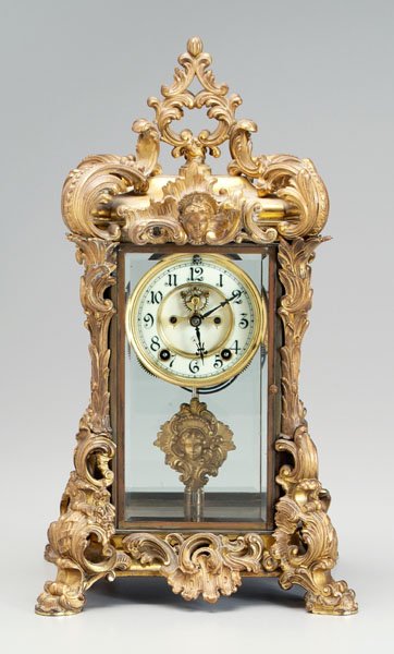 Ansonia baroque style clock,: scrolled decoration with female head pediment, bronze dore mounts, original pendulum and key, 18-1/2 in. Retains some original dore surface, one base mount loose.