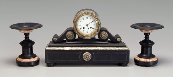 Slate and marble shelf clock,: circular clock housing flanked by two scrolls with marble highlights, face with indistinct marking, key wind, probably French, circa 1900, 11-3/4 x 17-3/4 x 6 in.; with two similar tazzas, 8-1/2 in. M