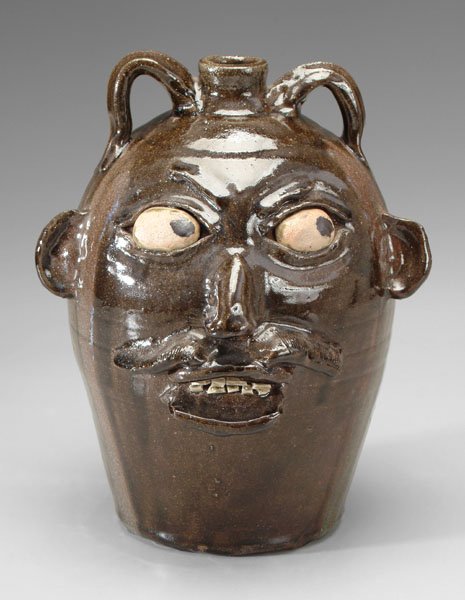 Chester Hewell stoneware face jug,: painted eyes, broken china teeth below an exuberant mustache, intended glaze runs, base marked "Chester Hewell 1985" (Gillsville, Georgia, born 1950), 14 in. Excellent condition.