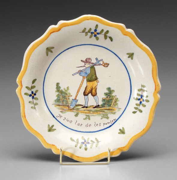 French faience bowl,: central scene with man carrying a sword, a cross and a shovel in fenced landscape above motto [Je suis las de les porter] (I am weary of carrying), late 19th/early 20th century, 1-1/4 x 10 in. Several