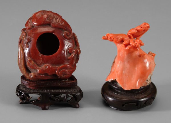 Two Chinese carved items:: base of coral branch carved as the Three Wise Monkeys seated in a tree, mounted to wood stand, 3 in.; red jasper water pot, carved as a peach on the end of a flowering branch, a bat at one end, 1-1/4 