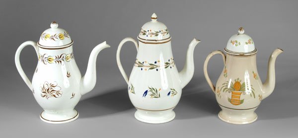 Three pearlware coffeepots: one with yellow and brown decoration, 10-3/4 in., [repairs to spout and rims, repaired crack, scattered retouch;] one with bands of green, blue and ocher flowers, 11-1/2 in., [repaired handle crack an