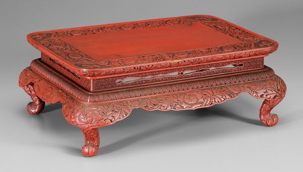 Chinese cinnabar lacquer low table,: rectangular top on stepped and waisted base with [ruyi]-head aprons, cabriole legs, carved with peonies, ground patterns of star, cube and diamond, late 19th/early 20th century, 6-1/4 x 17-1/4 x 12-1/