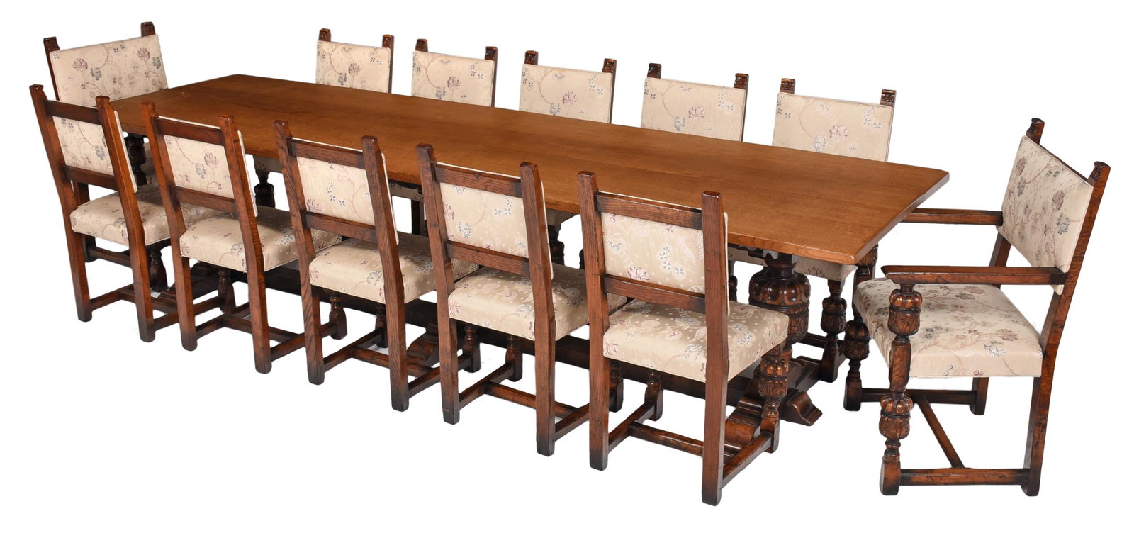 Jacobean Style Carved Oak Upholstered Dining Suite: early 20th century, the oak table with trestle base with boldly carved supports, the matching two arm and eight side chairs upholstered in floral silk fabric, 38-1/2 x 19 x 21 in. chairs and 31 x 126 