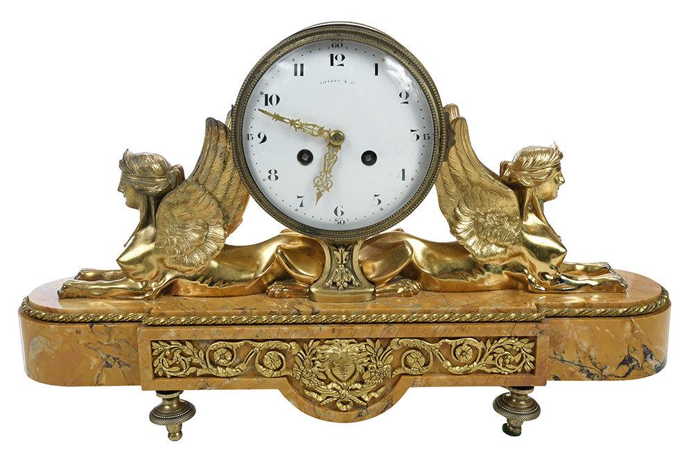 Tiffany & Co. Gilt Bronze and Marble Mantel Clock: French, 19th century, porcelain dial with Arabic numerals, marked "Tiffany & Co." and "France", supported by two opposing gilt bronze sphinxes, raised on a shaped marble plinth, with winder key, 11-5/