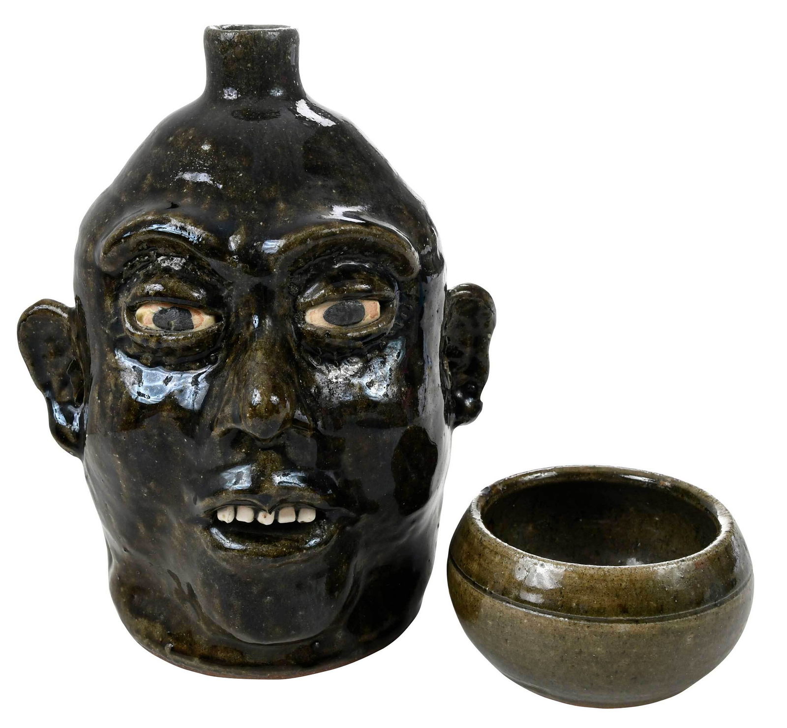 Lanier Meaders Face Jug, and Small Bowl: (White County, Georgia, b. 1917, d. 1998) face jug with dark runny olive green glaze, white clay teeth and eyes, painted black pupils, applied facial features, pronounced cheeks and chin, straight spo