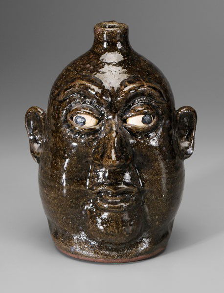 Lanier Meaders Face Jug: Georgia, 20th century, stoneware, glossy olive glaze, distinct cheeks, ceramic eyes, base incised "Lanier Meaders", (White County, Georgia, 1917-1998), 10-1/2 in., good condition, firing crack at left