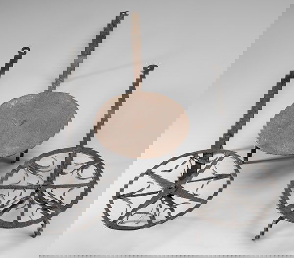 Three Wrought Iron Revolving Trivets: two with arched decoration, tripod bases, one with stepped handle; one with solid circular platform, four feet, 21-7/8 in. to 28 in., all with old black-painted surfaces over light rust and losses Pro