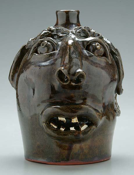 Stoneware face jug,: snake wrapped around top with eyebrows, bulging eyes, broken china teeth, runny brown glaze, base marked "Brown's Pottery, Robert Brown", 8"