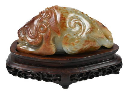 Finely Carved Chinese Jade of Hardstone Mythical Beast: pale green color with russet inclusions, crouching beast with open mouth, horns, curly mane and large feathery tail, nubby spine, 1-1/2 x 1-1/4 x 2-7/8 in.; on fitted wooden stand with accession