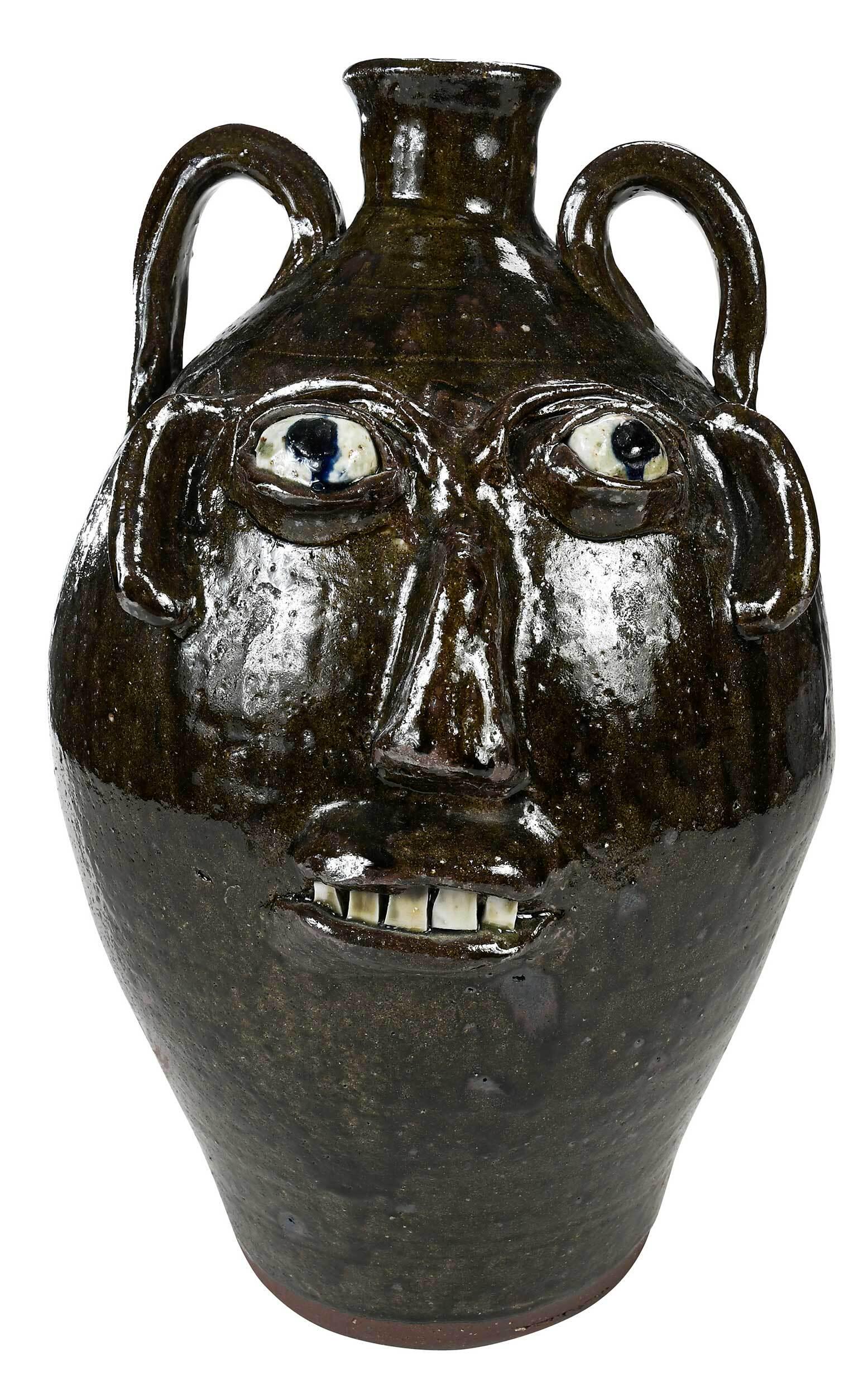 Large Burlon Craig Face Jug: (Vale, North Carolina, 1914-2002) runny olive green alkaline glaze, applied facial features, white kaolin eyes, blue painted pupils, broken china teeth, wavy line decoration between large applied stra
