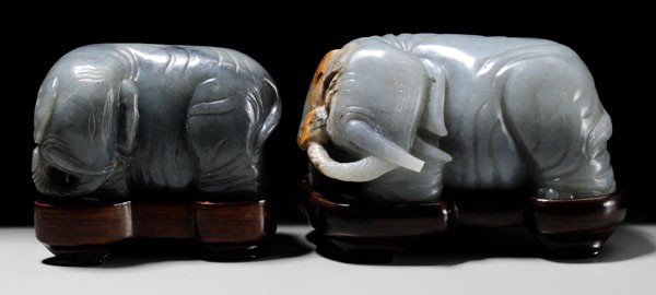 Two Jade Elephants: Chinese: each carved with heads turned to the left, trunks curling under tusks and up to right ear, one celadon with black inclusions, 2-1/2 x 4-1/8 x 2-1/4 in., with fitted wood stand, [jade excellen