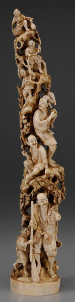 Ivory [Okimono]: Japanese, late 19th/early 20th century, carved to conform to natural shape of tusk, several figures sitting in a tree, a hunter holding a gun with young boy and dog at the base of the tree, a monkey o