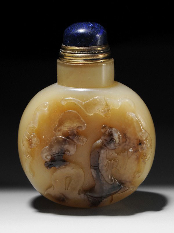 Agate Snuff Bottle: Chinese, 19th century, body carved with [lohan] beside rock formation with [lingzhi] fungus, three bats in the air around him, [lapis lazuli] stopper, 3 in., very minor chip to hand of [lohan] Provena