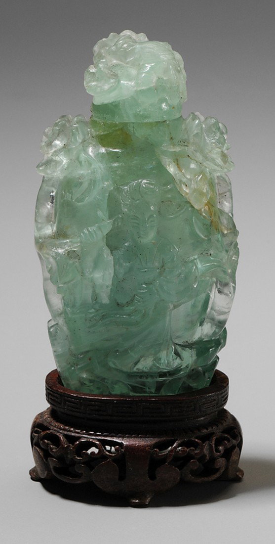Green Stone Snuff Bottle: Chinese, 19th century, tourmaline or beryl, carved with He Xiangu holding a lotus flower, verso with two birds, sides and stopper carved with flowering plants, with wood stand, 3-1/4 in., minor chips 