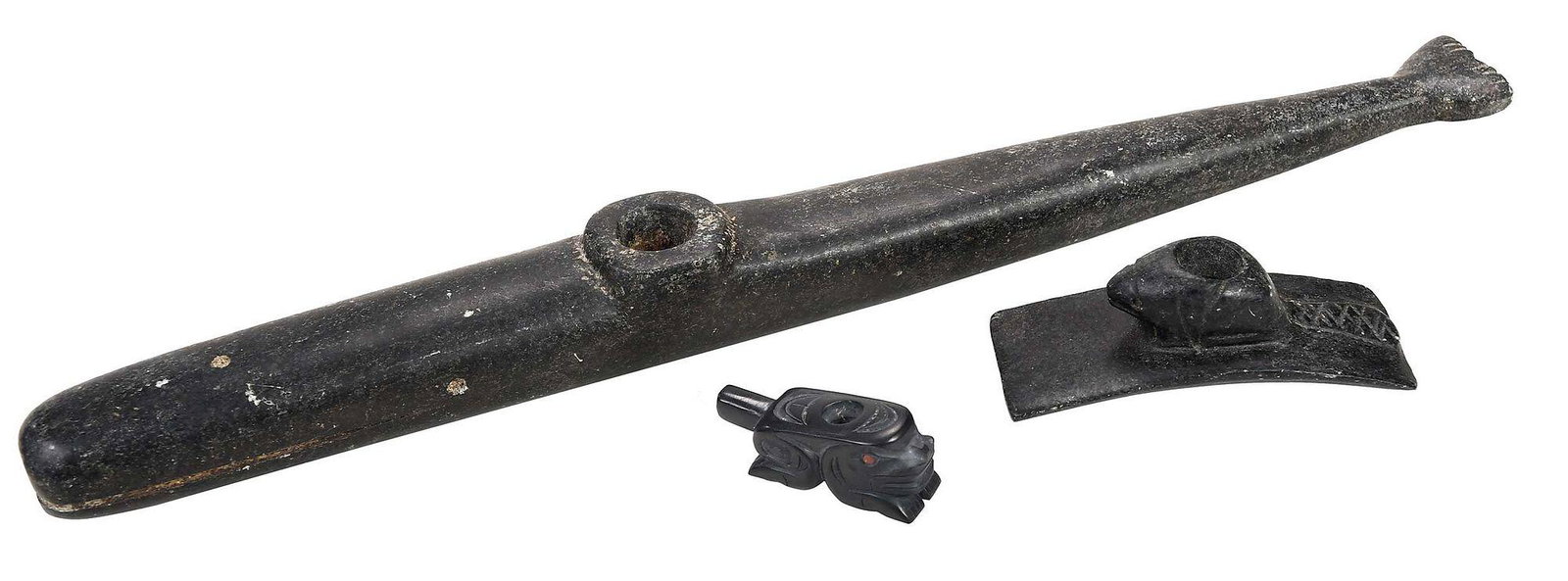 Three Carved Northwest Coast Pipes: all 20th century, the first a carved and incised frog effigy pipe by Norman Russ, (Haida, born 1963), signed on base "norm russ", carved slate, red painted eyes, 2 in. long; together with a carved and