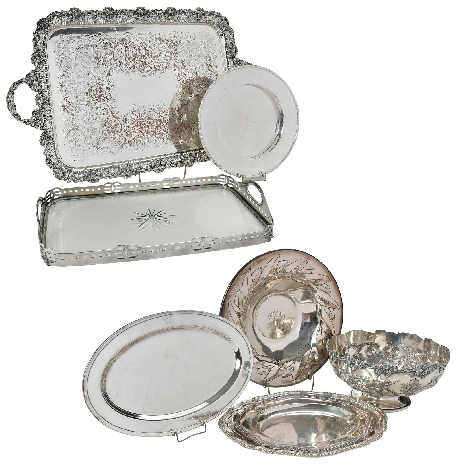 Eight Silver Plate Table Items: 20th century, including large footed bowl with grape decoration; large two handle tray with open work border; Art Deco gallery tray with glass floor; oval tray; two Georgian style trays; round plate w