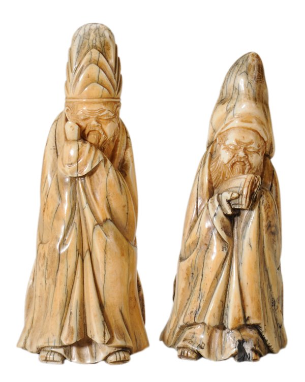 Two Mastodon Ivory Carved Figures: of Standing Scholars probably Chinese, 19th century, mastodon ivory figures of standing scholars, each dressed in elaborate cap and robe, one holding a book, the other possibly a scepter or page turne