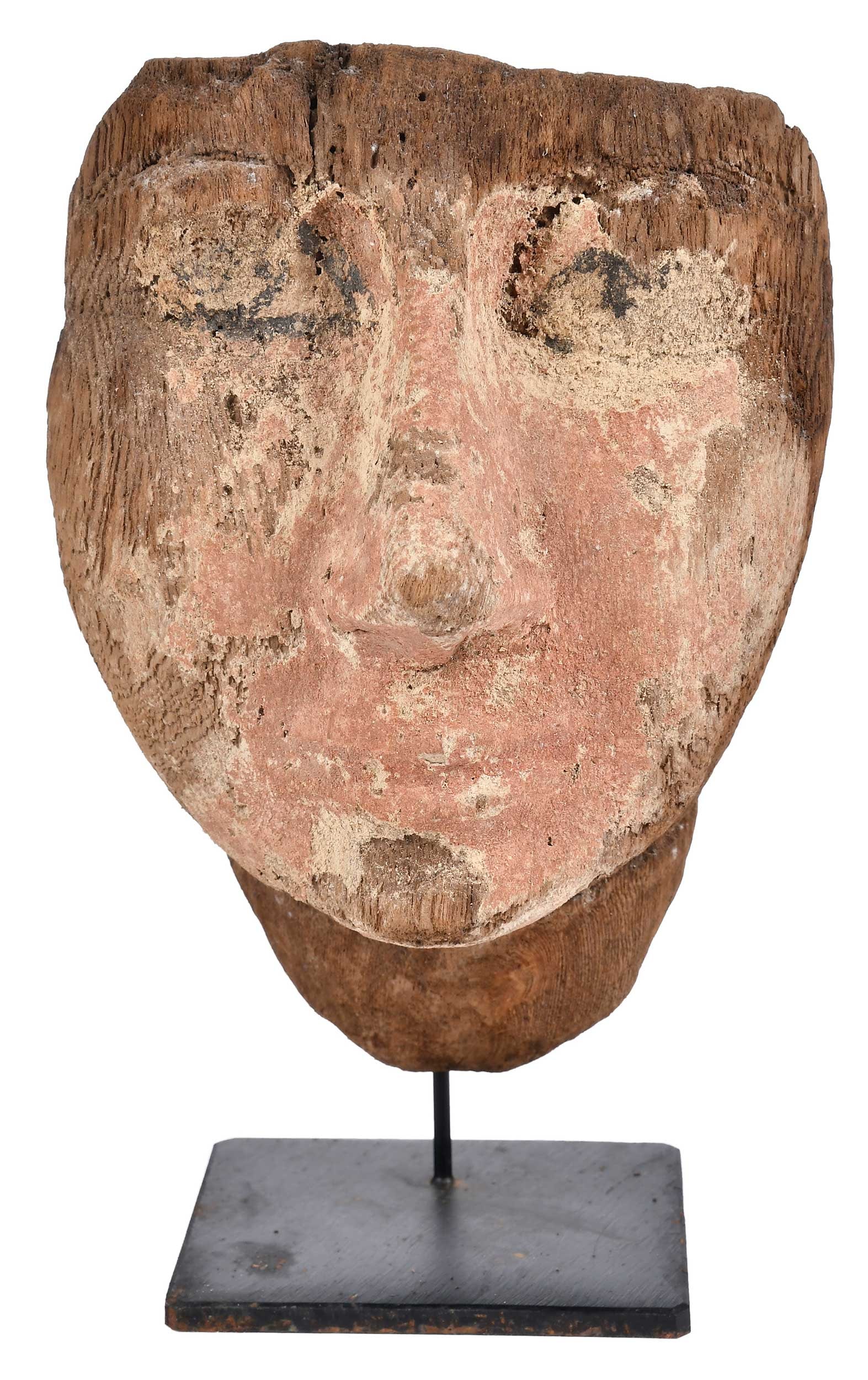 Egyptian Carved and Painted Wood Mummy Head: possibly Late Dynastic period, face with remnant brick red paint, neutral expression with wide remnants of white and black painted eyes, two peg remnants in top upper section verso, mounted with screw