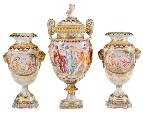 Three Capodimonte Urns: Continental, 20th century: pair with oval panels depicting classical scenes with nude figures, ram's head mounts, rim and shoulders with red and green leaf borders, gray-printed crown-over-N mark, 10-