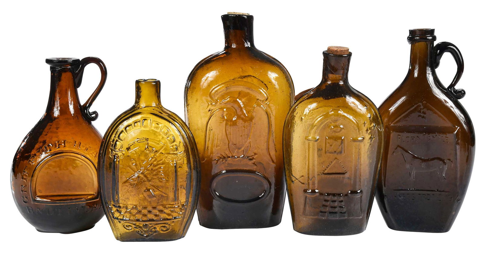 Five American Pictorial Brown Glass Flasks: American, 19th century, various forms with eagle, star, and other symbolic motifs, including: "Griffith Hyatt & Co/Baltimore" example; "KCCNC" example; "Flora Temple/Harne