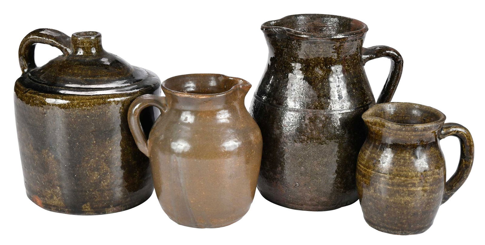 Four Pieces of Cheever Meaders Attributed Pottery: large pitcher, stacker jug, and creamer with dark olive green alkaline glazes, applied strap handles, 9, 8-1/4, and 5-1/2 ins. tall; pitcher with brownish olive green alkaline glaze, applied strap han