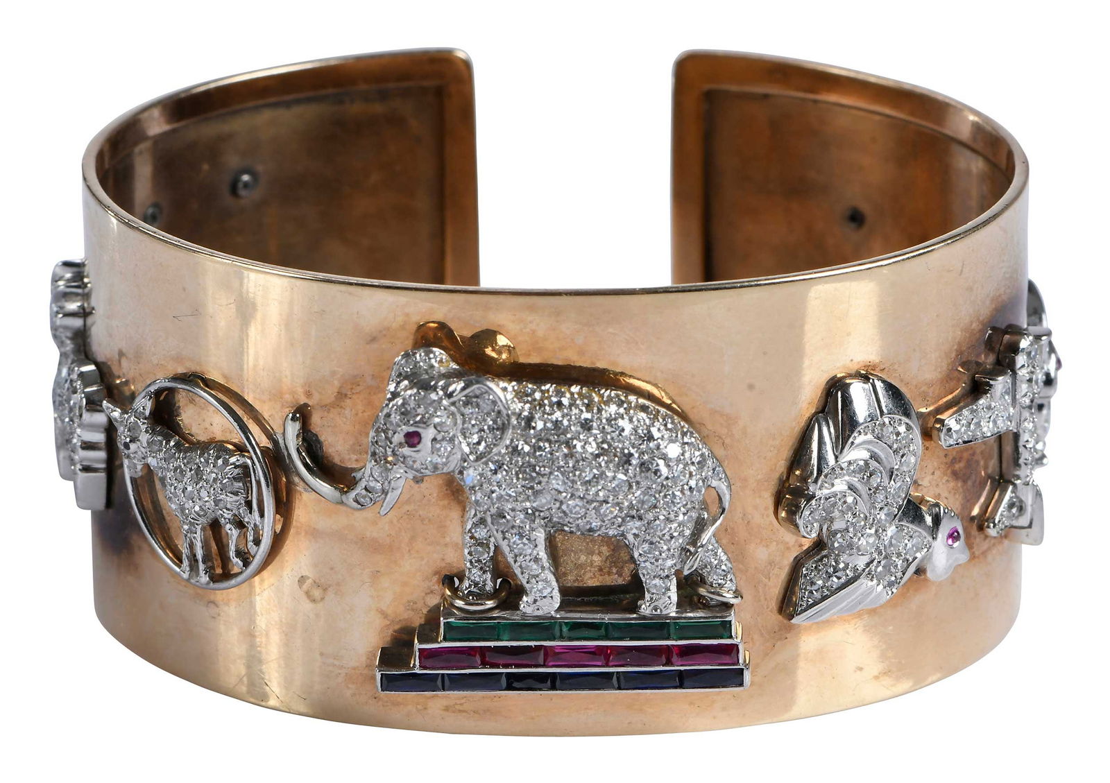 14kt. Wide Diamond and Gemstone Cuff Bracelet, Bush Family Provenance: ?nine charms, all accented with round full cut and single cut diamonds; dog with round coral eye, four carved leaf emeralds, pheasant with round ruby eye, goat, lamb with ruby eye, elephant with round