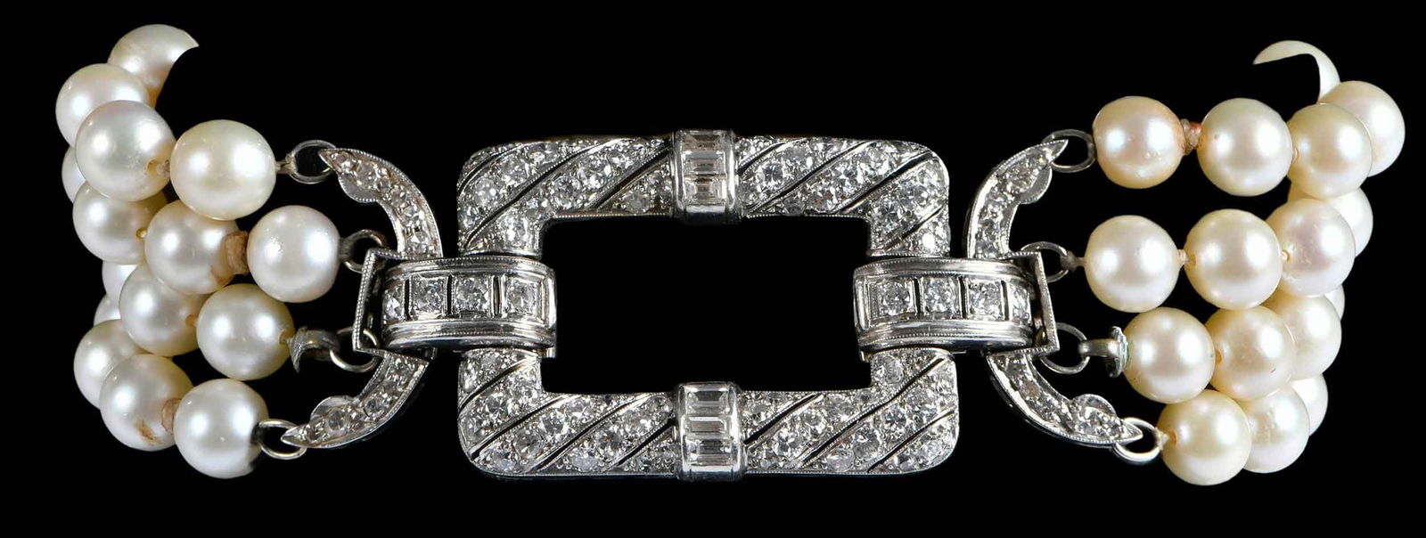 18kt. Art Deco Diamond Clasp and Multi Strand Pearl Bracelet, Bush Family Provenance: round brilliant cut and straight baguette diamonds in clasp, 1-3/4 in. length, 21.0 mm wide, attached by four strands of 5.5 - 6.5mm white pearls, tests 18kt. white gold, 7 in. total length, 41.6 g Pr