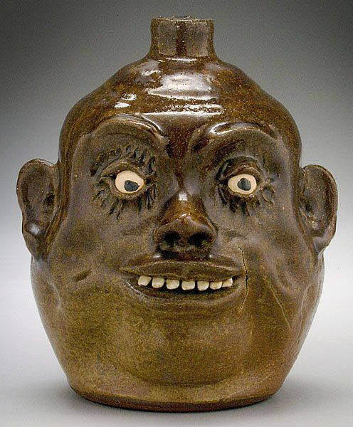 Lanier Meaders stoneware face jug,: Lanier Meaders stoneware face jug, glossy medium to light olive alkaline glaze, ceramic teeth, bulging eyes, base inscribed "Lanier Meaders," 9-1/2 in. Firing flaws and glaze blisters, firing crack (a