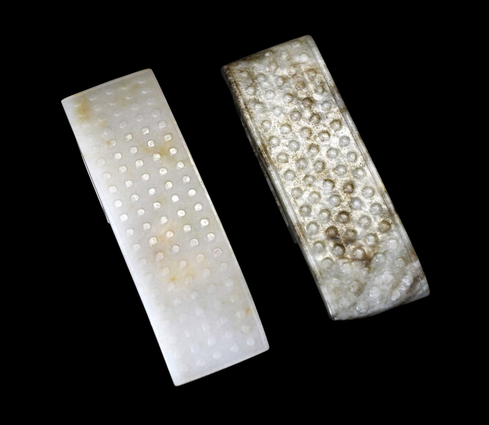 Two Chinese Carved Jade Sword Fittings: jadeite fitting, whitish with russet inclusions, 4 x 1-1/4 x 1/2 in.; nephrite fitting, pale green with brown inclusions, 3-3/4 x 1-1/4 x 1/2 in. Provenance: The Collection of William S. Arnett,