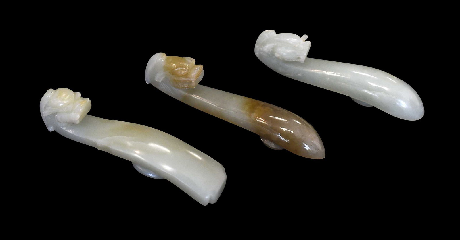 Three Chinese Carved Jade Dragon Belt Hooks: each pale green, one with brown inclusions, largest 3-5/8 x 3/4 x 1 in. Provenance: The Collection of William S. Arnett, Atlanta, Georgia; sold to benefit Tinwood Foundation Note: These items test as 