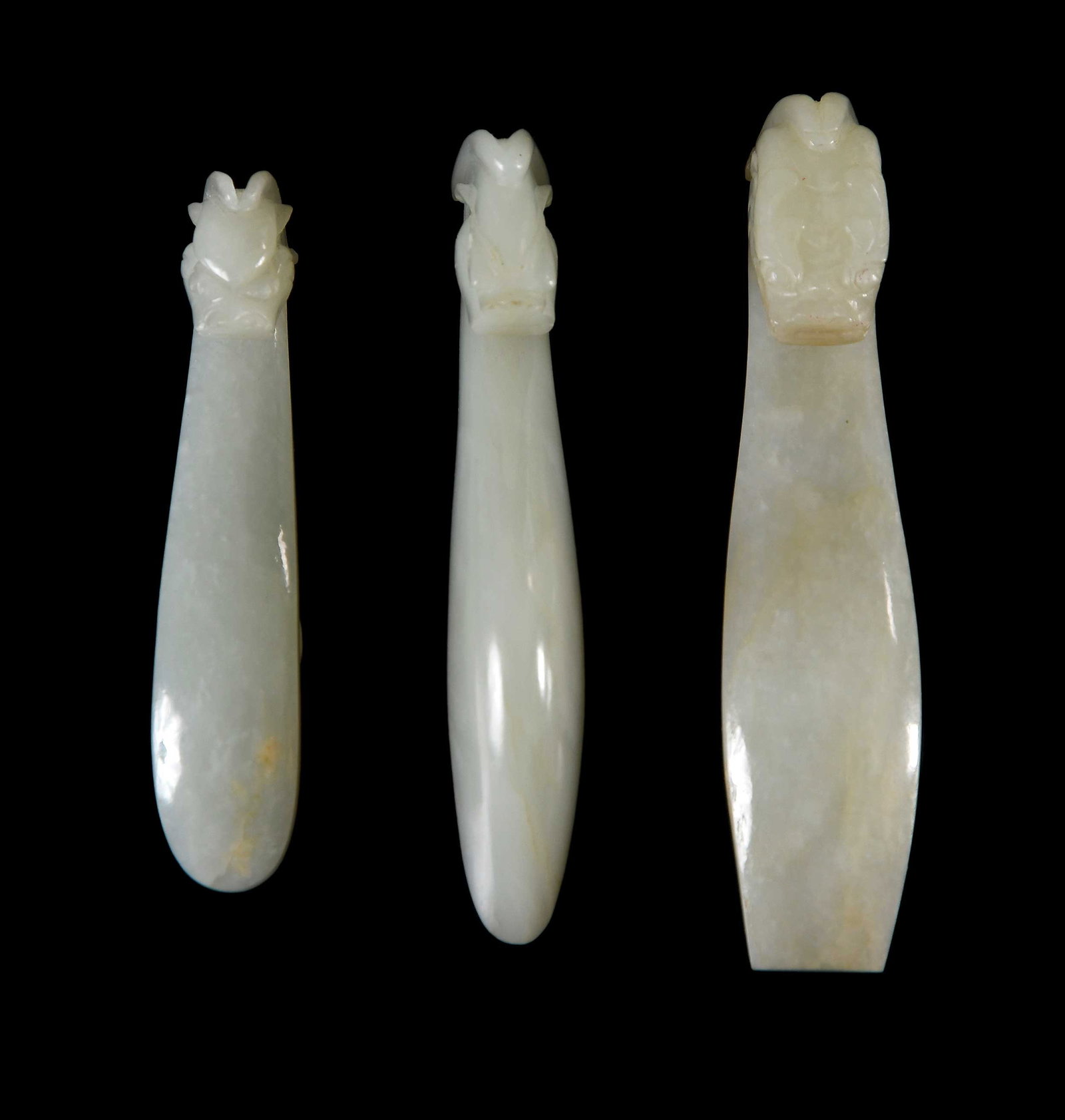 Three Chinese Carved Jade Belt Hooks: all with qiulong (horned dragon) head motif in pale celadon jade, two with some mottling and white and/or tan inclusions, largest 4-1/4 x 1 x 7/8 in. Provenance: The Collection of William S. Arnett, A