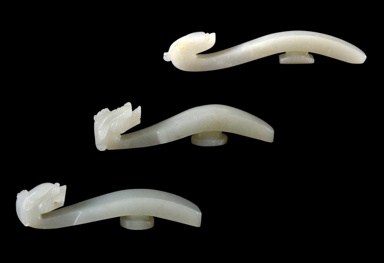 Three Chinese Carved Pale Celadon Belt Hooks: each with carved dragon/chilong head, largest 4-1/4 x 1/2 x 3/4 in. Provenance: The Collection of William S. Arnett, Atlanta, Georgia; sold to benefit Tinwood Foundation Note: These items test as neph