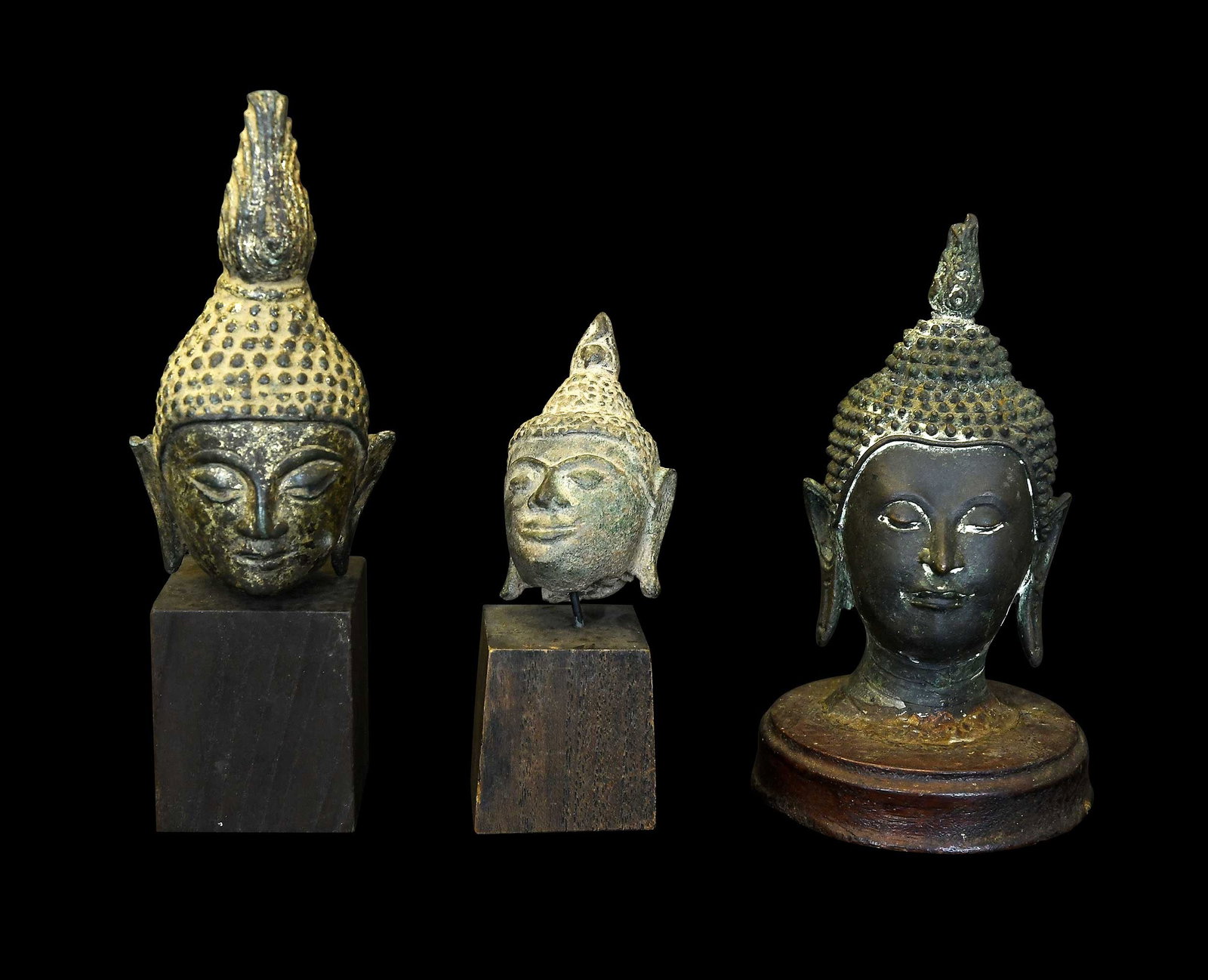 Three Miniature Southeast Asian Bronze Buddha Heads: probably Thai, possibly 16th-18th centuries, mounted on wood bases, largest 6 x 1-1/2 x 1-1/2 in. including base Provenance: The Collection of William S. Arnett, Atlanta, Georgia; sold to benefit Tinw