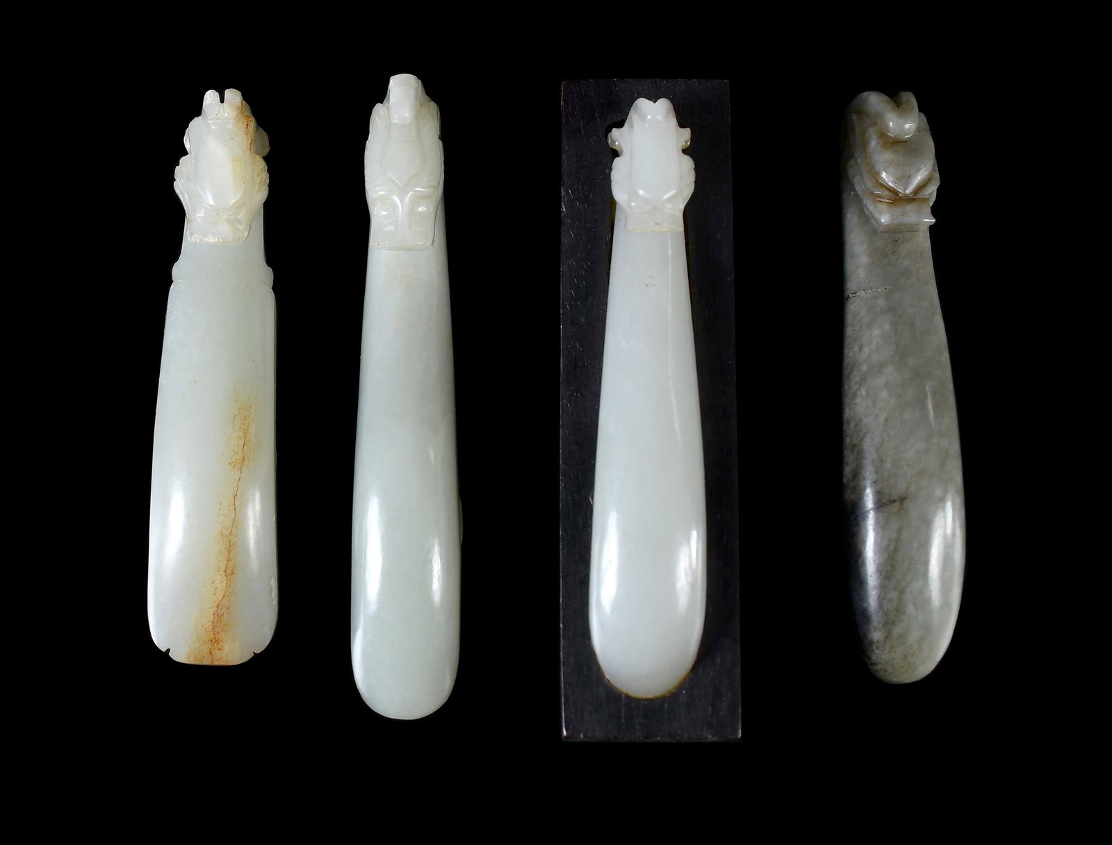 Four Chinese Carved Jade Dragon Belt Hooks: each pale green, one attached to wood stand, largest 1-1/4 x 3-1/2 x 7/8 in. Provenance: The Collection of William S. Arnett, Atlanta, Georgia; sold to benefit Tinwood Foundation Note: These items