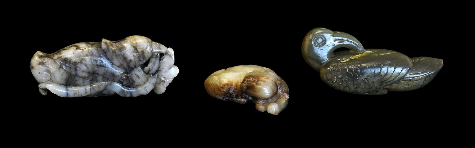 Three Chinese Carved Jade Recumbent Animal Figurines: comprising: parrot in olive green with russet inclusions; bird with flower in grey with black inclusions; fu lion in celadon with russet inclusions; largest 1-1/4 x 3 x 1 in. Provenance: The Collectio