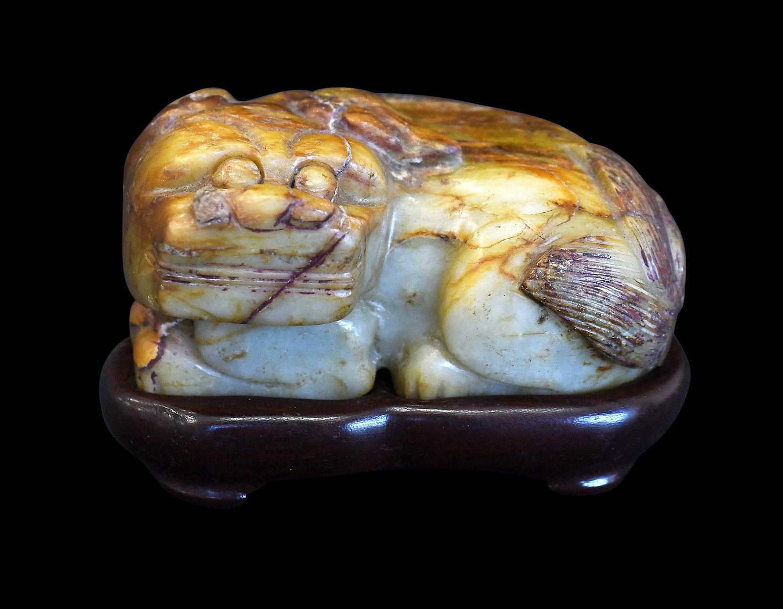Chinese Carved Jade Foo Dog on Stand: green with orange and russet inclusions, 1-7/8 x 3-1/2 x 2-1/4 in.; fitted carved wood stand, 3/4 x 3-1/2 x 2-1/8 in. Provenance: The Collection of William S. Arnett, Atlanta, Georgia; sold to