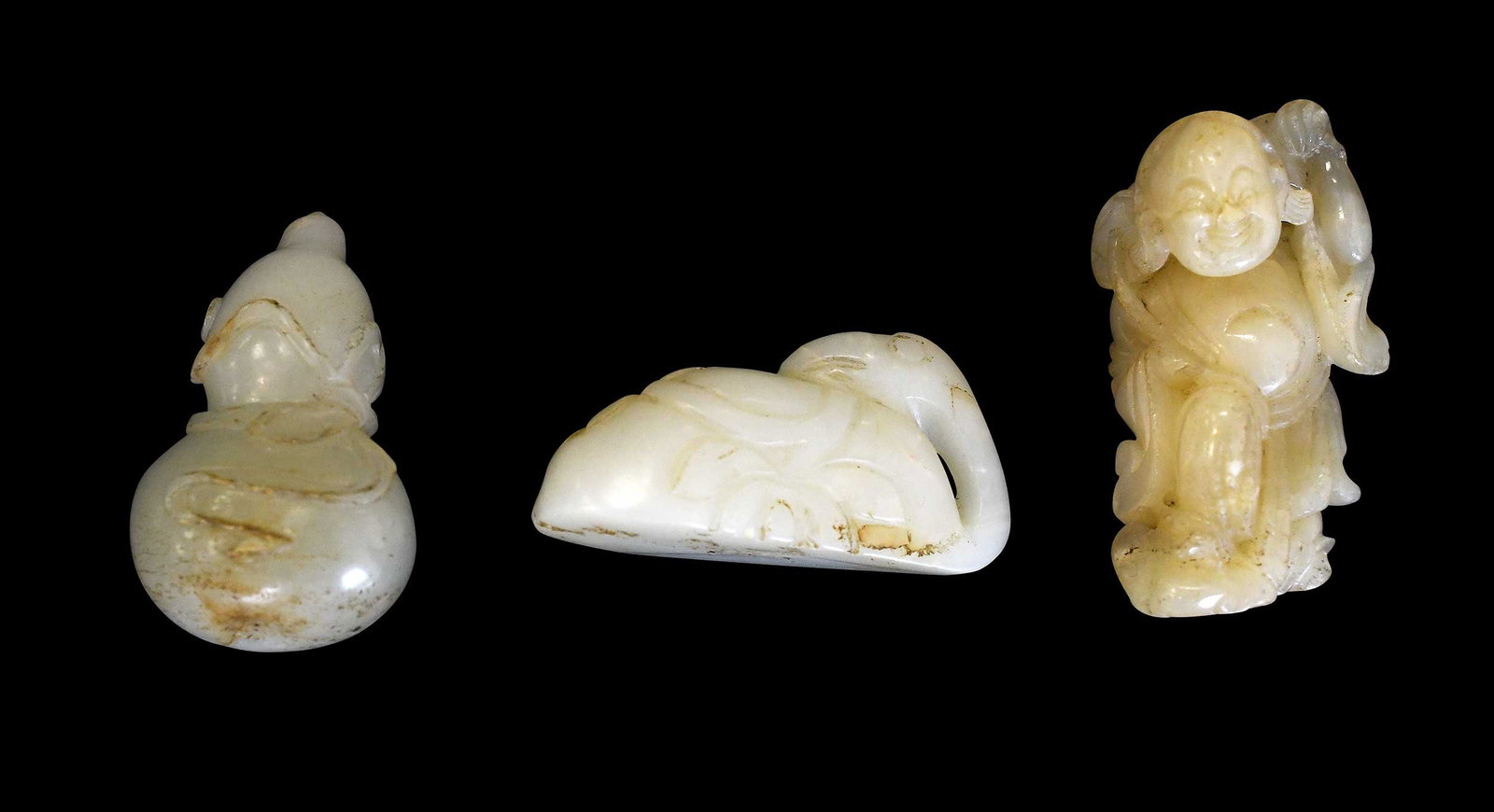 Three Chinese Carved Jade and Hardstone Figurines: two carved of pale green jade with russet inclusions, one of celadon hardstone, largest 3/4 x 2-1/4 x 1-1/4 in. Provenance: The Collection of William S. Arnett, Atlanta, Georgia; sold to benefit