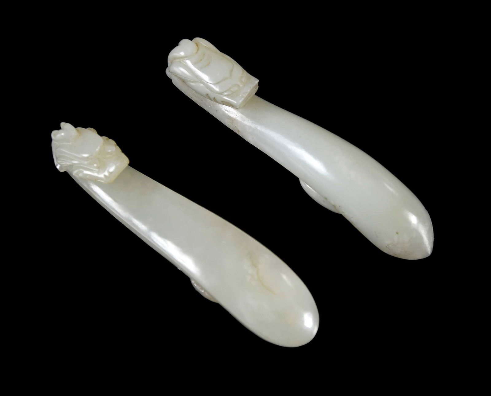 Two Small Chinese Carved Pale Green Jade Belt Hooks: each with carved dragon/chilong head, each approx. 3-1/8 x 5/8 x 5/8 in. Provenance: Charlottesville, Virginia Collection Note: These items test as nephrite on the Presidium Gem Tester II.