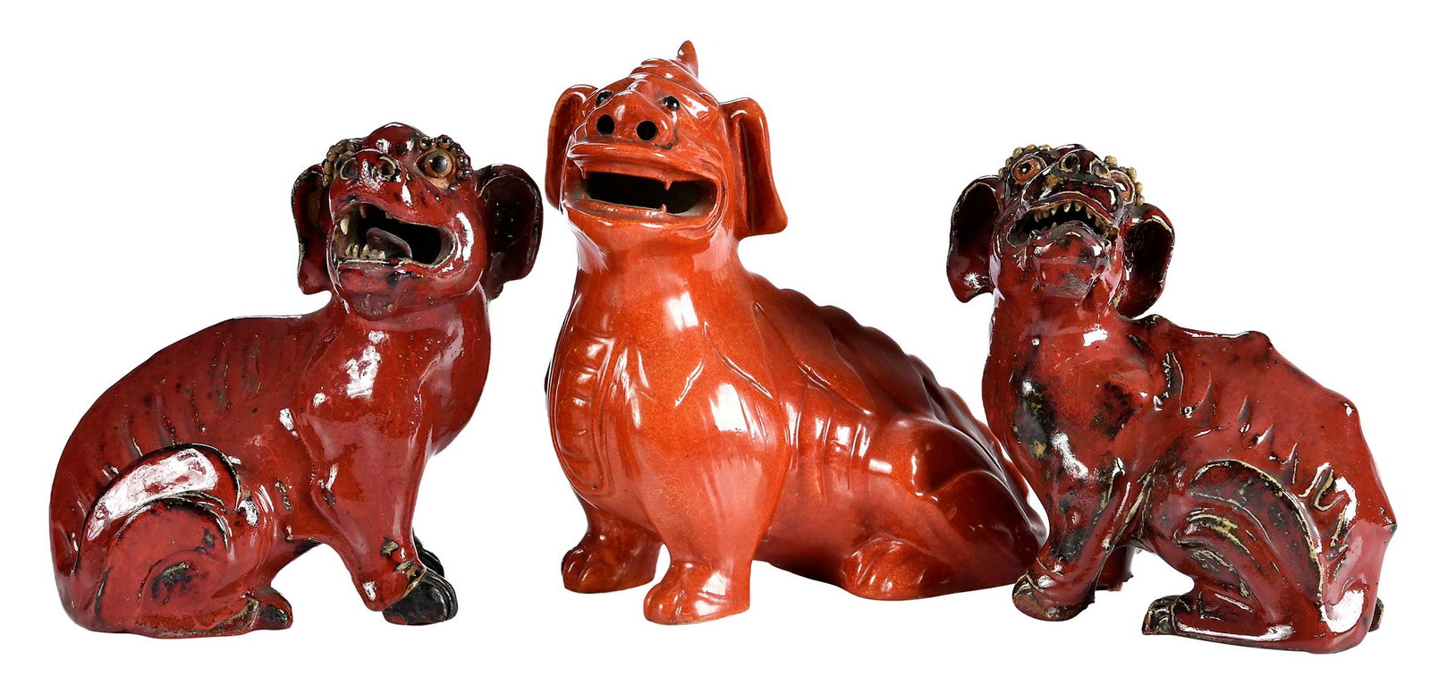 Three Chinese Export Temple Guardian Dogs: orange glazed porcelain sitting dog with single horn, black eyes; pair of earthenware dogs with red and black glaze, open mouths, 7 x 6-1/2 x 4 in. Provenance: The Collection of Joe Matthews and John
