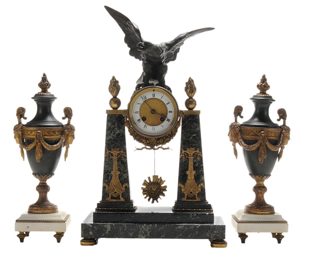 [Directoire] Marble and Ormolu Portico: Clock with Pair Urns French, early 19th century, clock with bronze wing spread eagle perched on the brass drum case, enameled and brass dial with Roman counters, marble supports with applied ormolu, f
