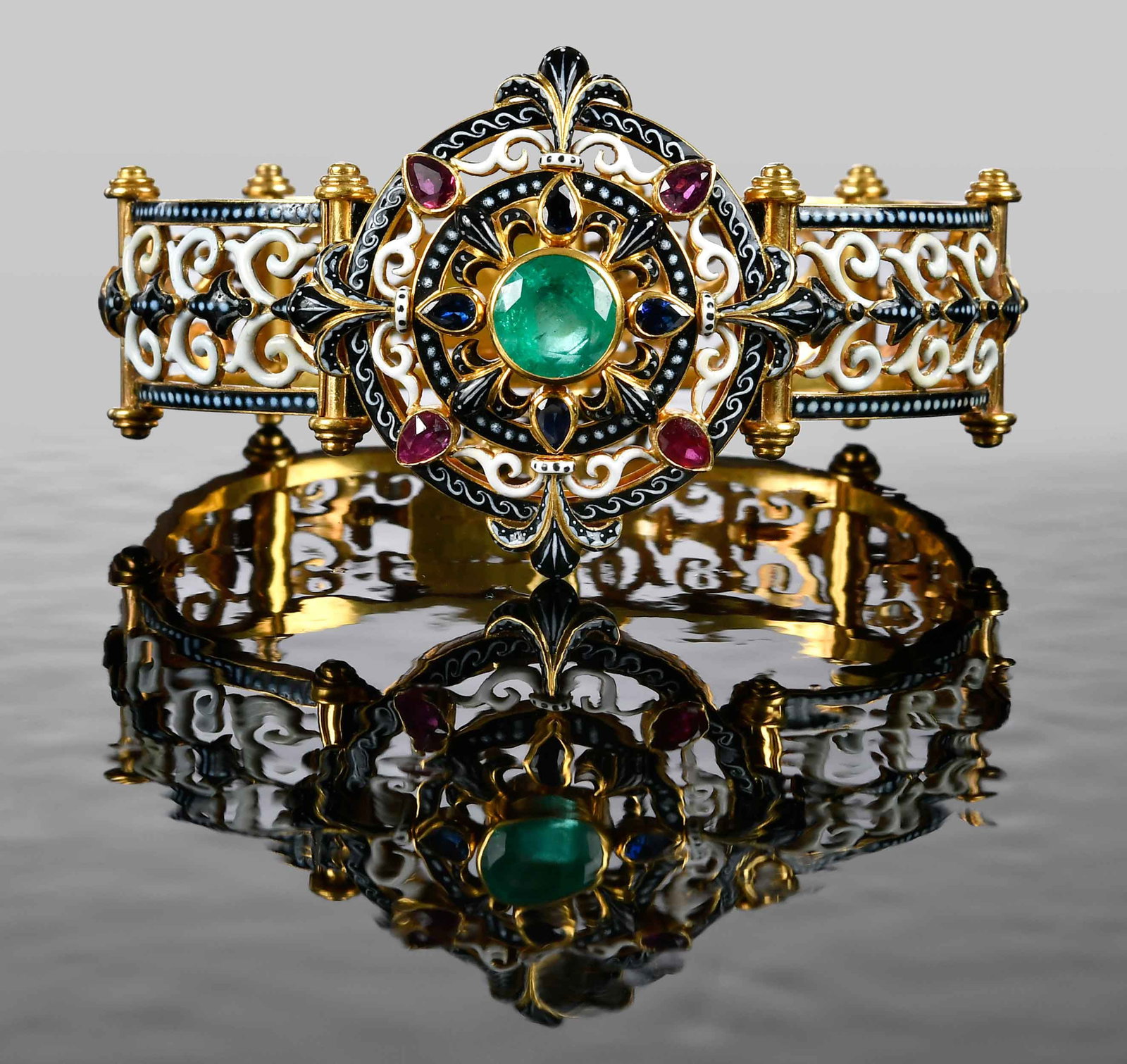 Carlo Giuliano Emerald and Enamel Bracelet, Original Fitted Leather Case: circa 1874, round faceted emerald, eight pear shape faceted rubies and blue sapphires, black and white enameled openwork scroll panels, signed "CG", for Carlo Giuliano, tests 18kt. yellow gold, origin