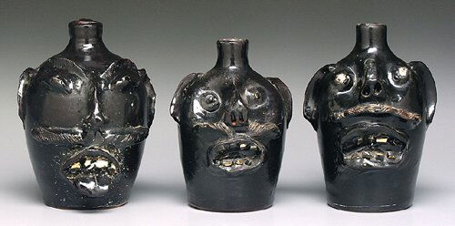 Three stoneware face jugs, black with mu: Three stoneware face jugs, black with mustaches, broken china teeth, one with tongue sticking out, marked on base "EJ Brown, Evans Hand Made" (Evan Brown Pottery, Arden, North Carolina), 6-1/2" to 7-1